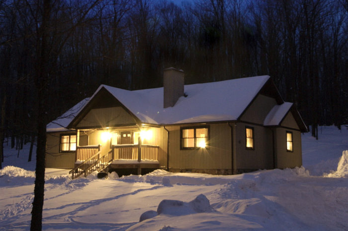 A cabin's interior lights glow against the snow outside on a cold winter night