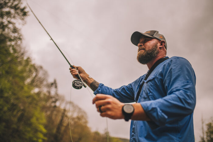 Medium shot of man casting a line in the water.