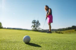 Close up of a rolling golf ball shot by a woman standing behind it.