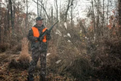 A hunter standing in the woods holding a deer rifle
