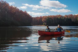 Father and son paddling in a canoe in a lake during the fall.