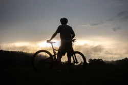 A mountain biker getting off his bike to watch a sunset.