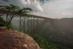 Angled view of the New River Gorge Bridge from a rocky edge during the summer.