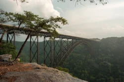 Angled view of the New River Gorge Bridge from a rocky cliff during the summer.