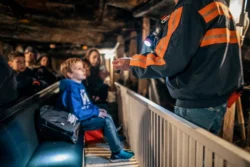 Wide shot of visitors aboard the mantrip underground as workers use supplies to demonstrate the history of coal mining.