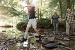 Family of three hiking across a stream in Tomlinson Run State Park during the spring.