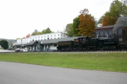 Wide shot of the Cass locomotive leaving the railroad station near the Company Store.