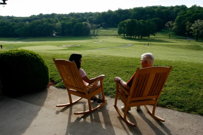Medium shot from behind a couple sitting in rocking chairs looking out at Cacapon Resort State Park.