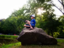 Child sitting on a large rock while fishing