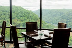 A set table with four chairs in front of a window with a scenic look over Hawks Nest State Park