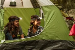Two children in a green tent with headlamps on, excited to camp.