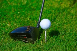 A golf club sitting next to a gold ball sitting on a golf tee.