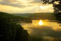 A view of the sun setting through the clouds and reflecting off of Summersville Lake