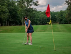 Person putting golf ball on green near hole with flag