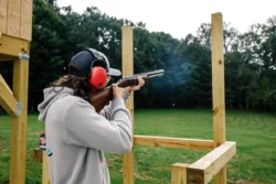 Person aiming shotgun at outdoor clay target shooting range